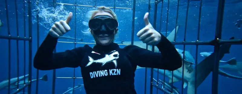 Plongeur souriant dans une cage avec des requins autour