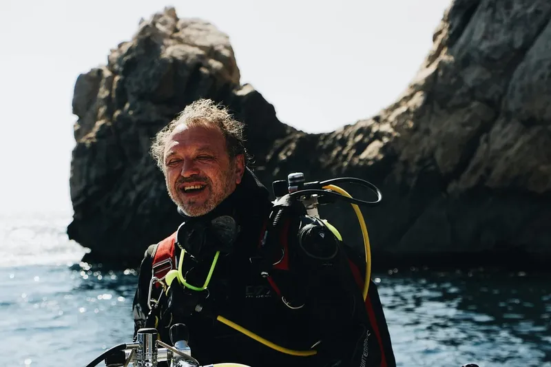 Plongeur souriant en combinaison, équipé, avec des rochers en arrière-plan