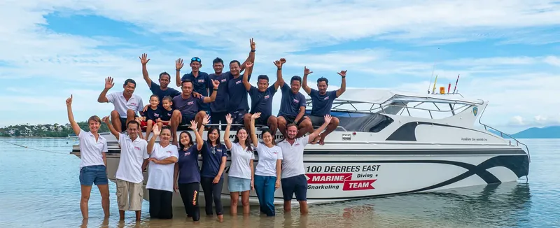 Equipe souriante posant devant un bateau de plongée sur une plage