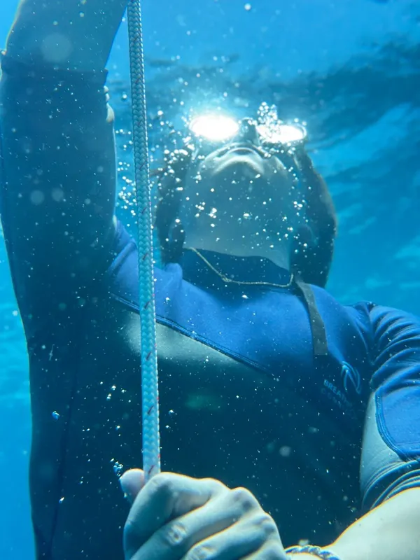 Plongeur en combinaison tenant une corde sous l'eau, regard vers le haut