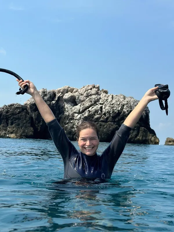 Femme souriante en combinaison de plongée, bras levés, en mer