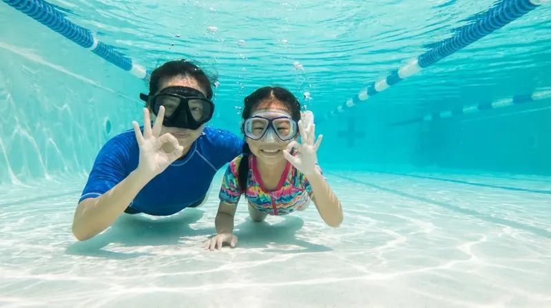 Deux personnes sourient et font des signes de la main sous l'eau