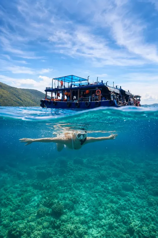 Plongeur nageant sous un bateau de plongée en eau turquoise claire