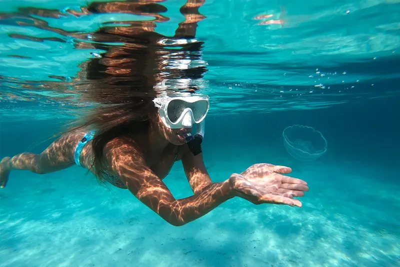 Femme nageant en apnée, bras tendu, eau turquoise et ensoleillée