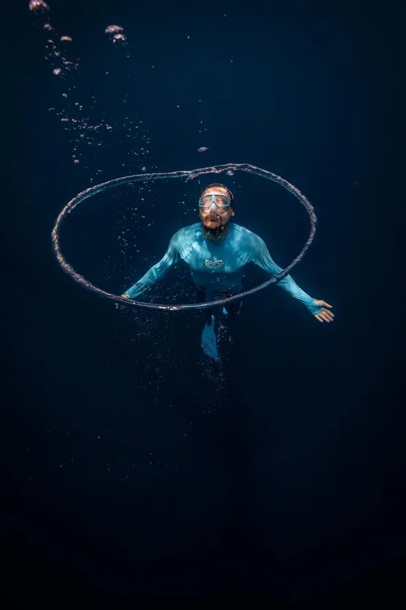 Apnéiste en combinaison bleue nageant avec un cercle sous l'eau