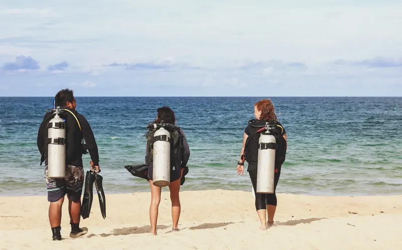 Trois plongeurs équipés regardent la mer depuis une plage de sable