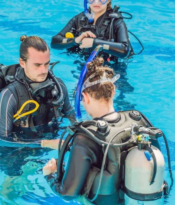 Trois plongeurs en formation dans une piscine, équipement complet visible