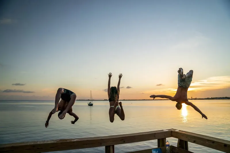 Trois personnes sautent d'un ponton au coucher du soleil en mer