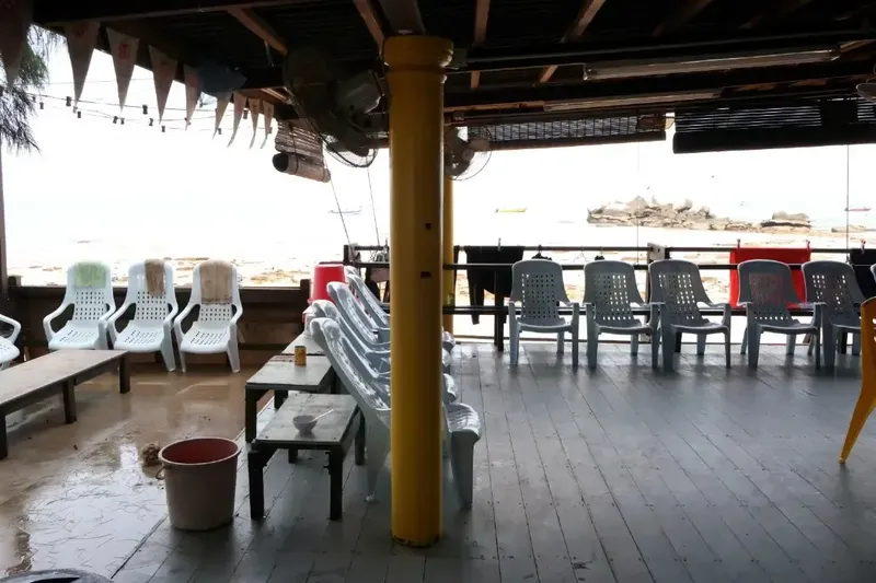 Terrasse ombragée avec chaises en plastique et tables basses vue sur mer