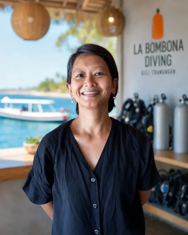 Femme souriante devant des équipements de plongée et un bateau