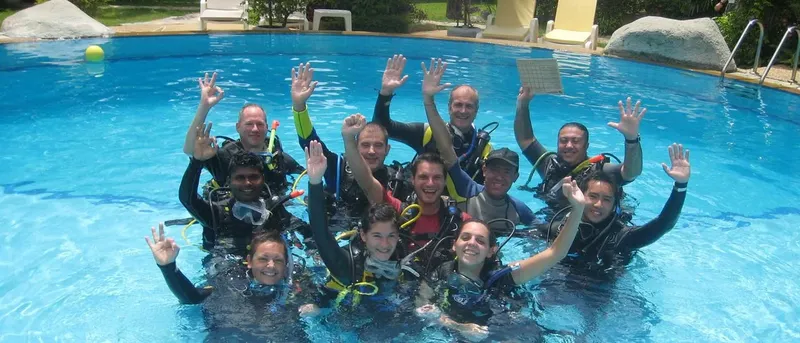 Groupe de plongeurs souriants en combinaison dans une piscine bleu clair