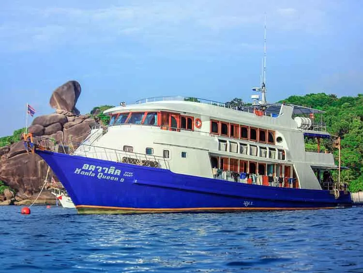 Grand bateau de plongée bleu et blanc amarré près d'îlots rocheux