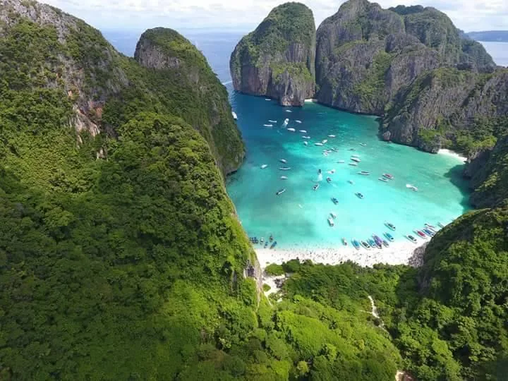 Vue aérienne d'une plage paradisiaque entourée de falaises verdoyantes et de bateaux