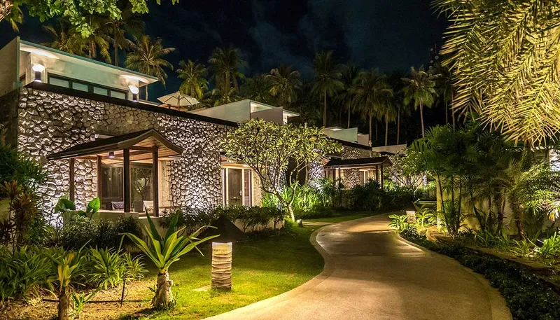 Bâtiments éclairés la nuit avec allée et végétation tropicale