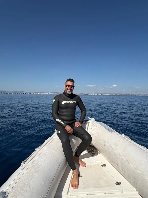 Homme en combinaison de plongée assis dans un bateau pneumatique bleu