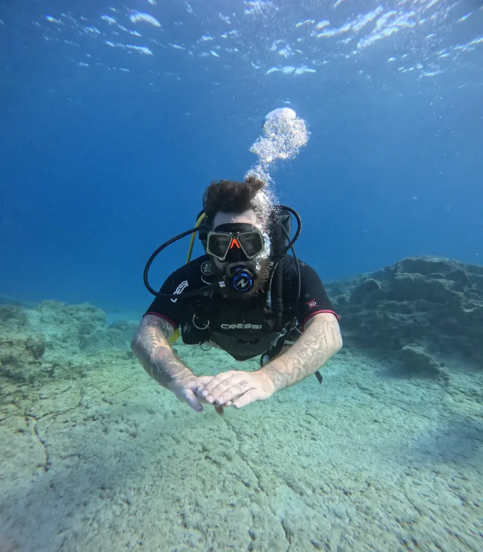 Plongeur en combinaison regarde la camera dans une eau claire