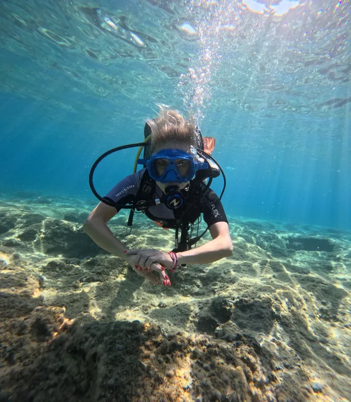 Plongeuse souriante, équipement complet, exploration sous-marine, fond sablonneux clair