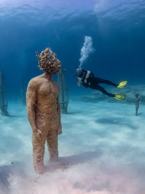 Plongeur explorant une sculpture sous-marine recouverte de vie marine