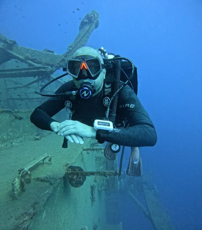 Plongeur en combinaison noire explore une épave sous-marine bleu profond