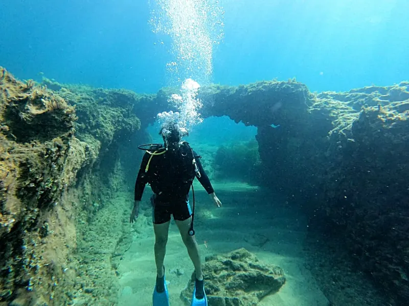 Plongeur explore une arche rocheuse sous-marine dans une eau claire