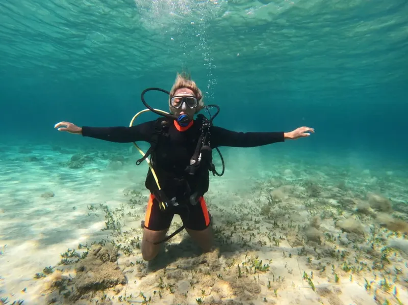 Plongeuse souriante, bras ouverts, au fond d'une mer claire et peu profonde