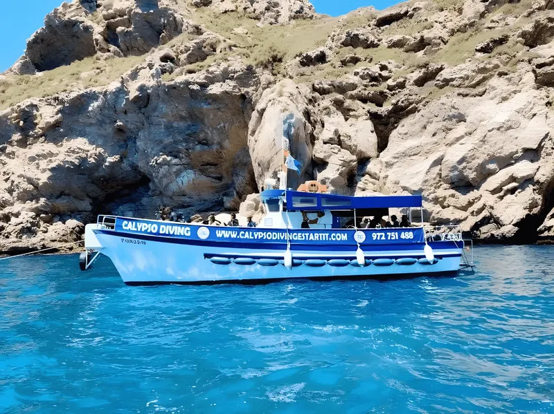 Bateau de plongée bleu et blanc amarré devant une falaise rocheuse