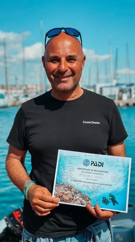 Un homme souriant tient un certificat de plongée PADI en main