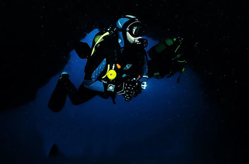 Plongeur en combinaison noire explore une grotte sous-marine sombre