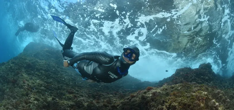 Apnéiste en combinaison nageant près d'une paroi rocheuse sous-marine