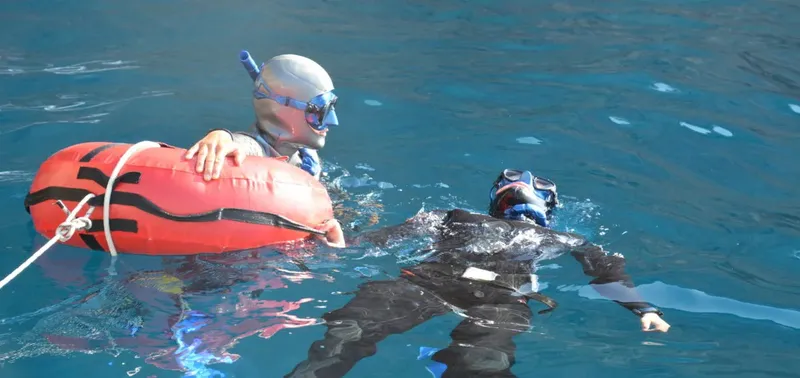 Deux apnéistes en combinaison flottent dans l'eau turquoise, l'un secourant l'autre