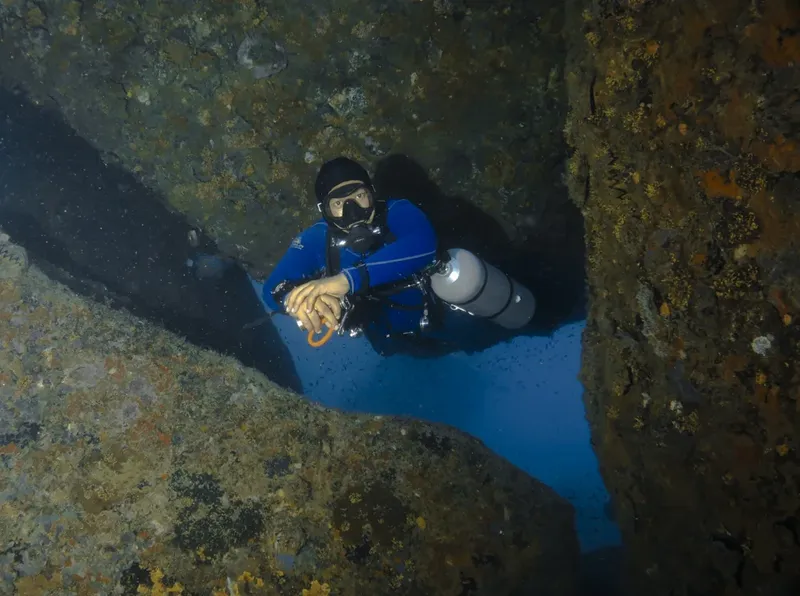 Plongeur explore une grotte sous-marine rocheuse avec une visibilité claire