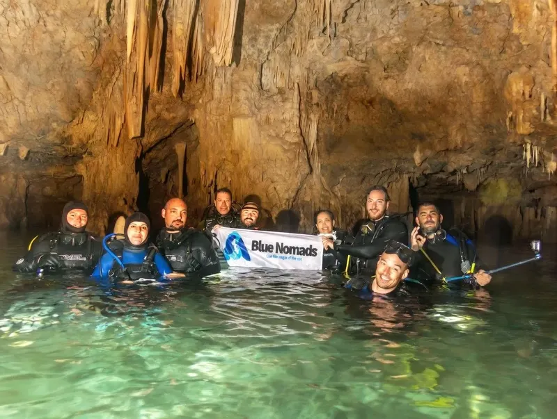Groupe de plongeurs souriants dans une grotte sous-marine avec une bannière
