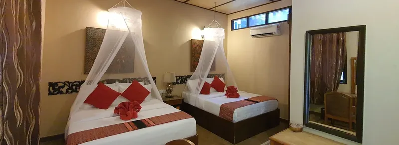 Chambre d'hôtel avec deux lits, moustiquaires et décoration tropicale