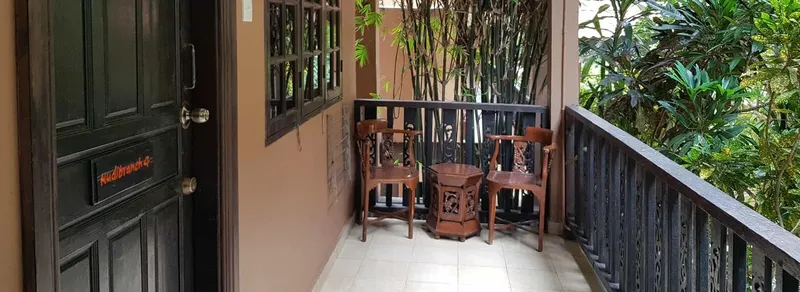 Balcon avec mobilier en bois, porte sombre et végétation luxuriante