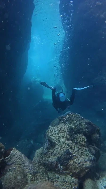 Plongeur explorant une faille rocheuse sous-marine avec lumière ascendante