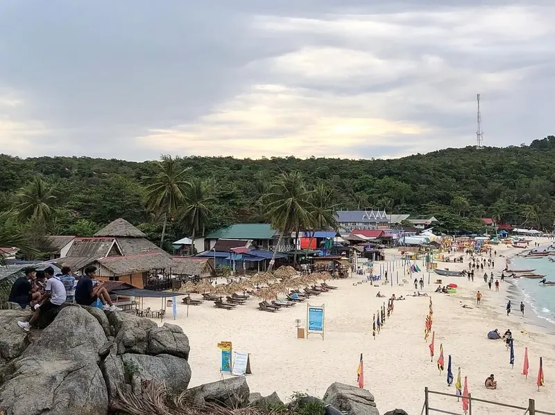 Plage avec des personnes, des bâtiments et des bateaux au loin
