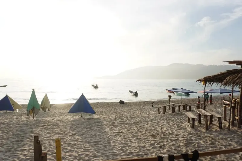 Plage avec quelques personnes, bateaux et abris de plage ensoleillés