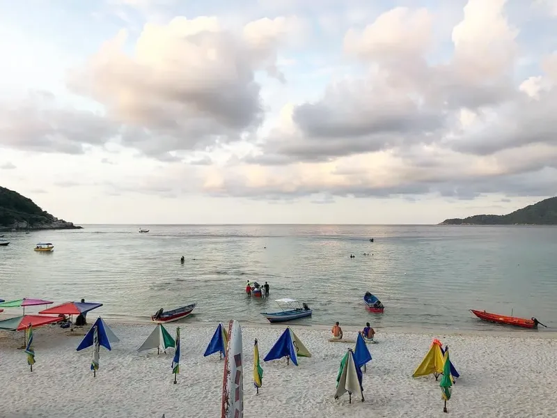 Plage avec des personnes dans l'eau et des bateaux au large