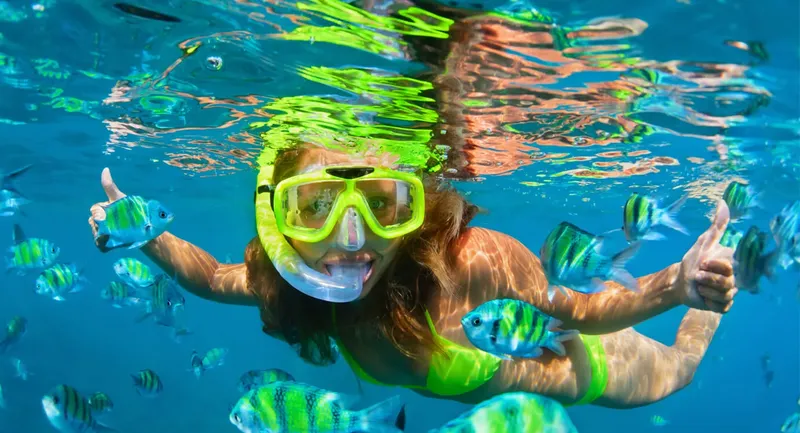 Plongeuse souriante entourée de poissons colorés dans une eau turquoise