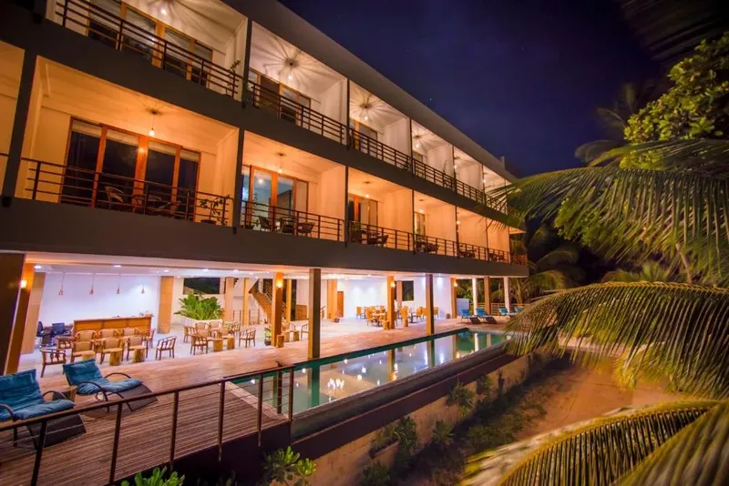 Bâtiment moderne avec piscine éclairée, végétation tropicale et ambiance nocturne