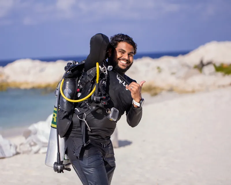 Plongeur souriant sur une plage, équipé de son matériel complet