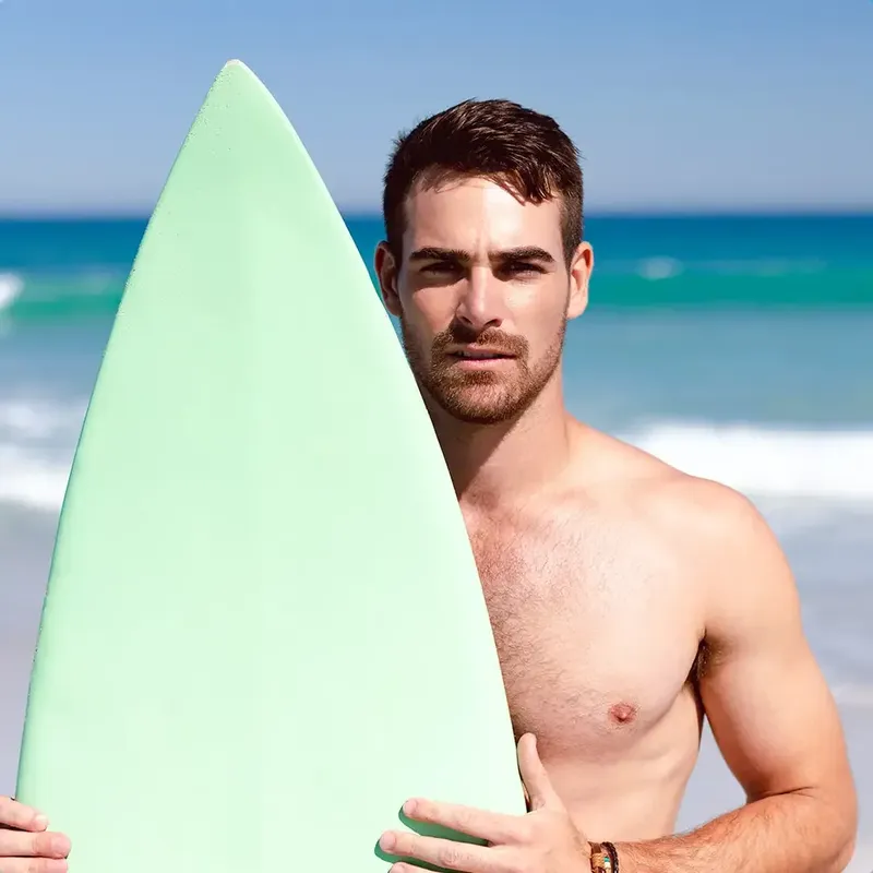 Jeune homme torse nu tenant une planche de surf sur plage