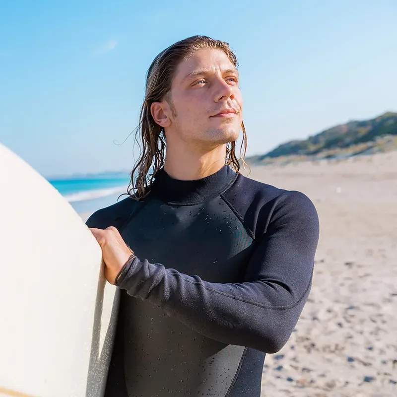 Un homme en combinaison de plongée regarde vers le ciel sur une plage