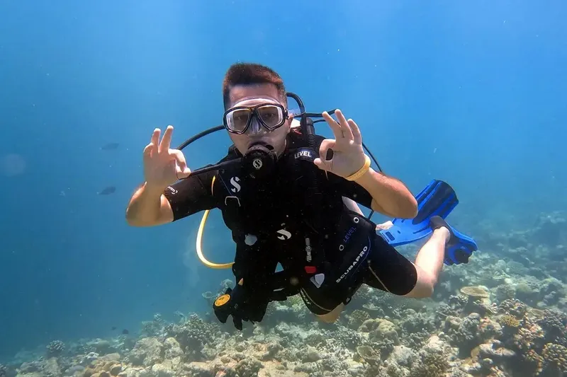 Plongeur souriant avec signe OK, en combinaison, dans l'eau bleue