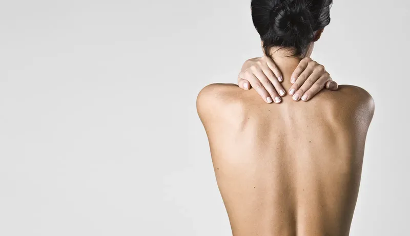 Femme vue de dos, mains sur les épaules, fond clair