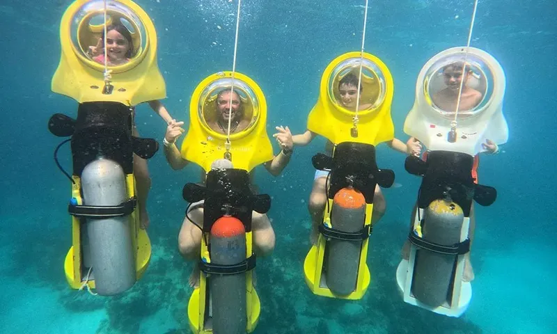 Quatre personnes sourient, équipées de casques sous-marins jaunes en plongée