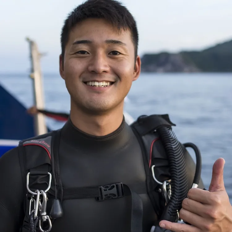 Plongeur souriant avec combinaison et détendeur, pouce levé, mer en arrière-plan