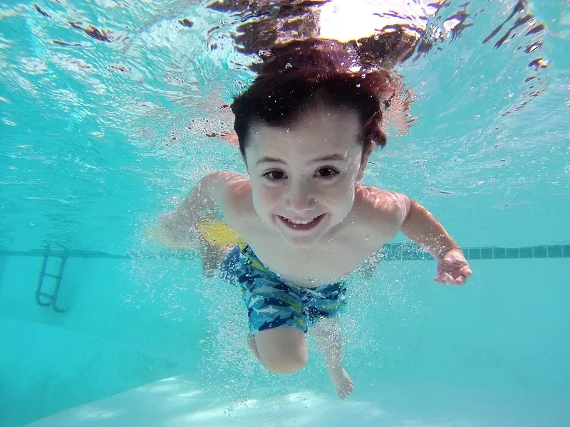 Enfant souriant nageant sous l'eau dans une piscine turquoise claire