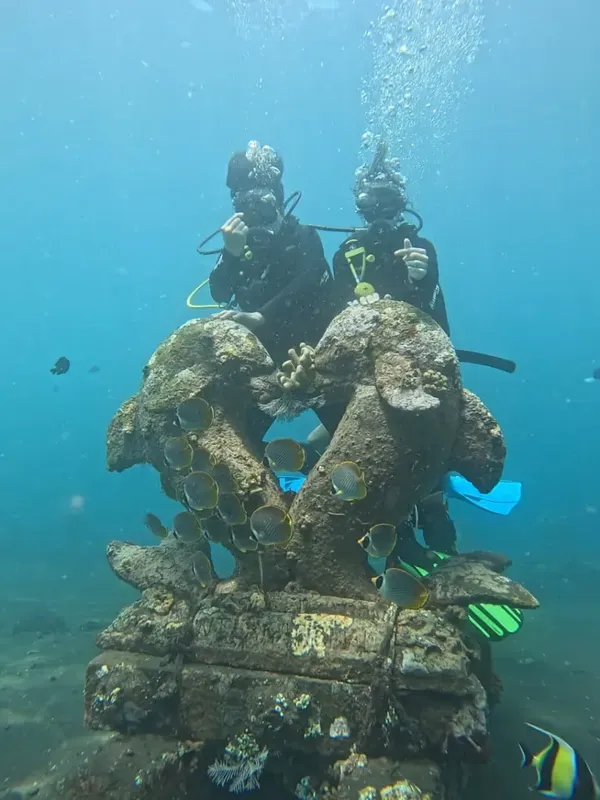 Deux plongeurs explorent une sculpture sous-marine colonisée par la vie marine