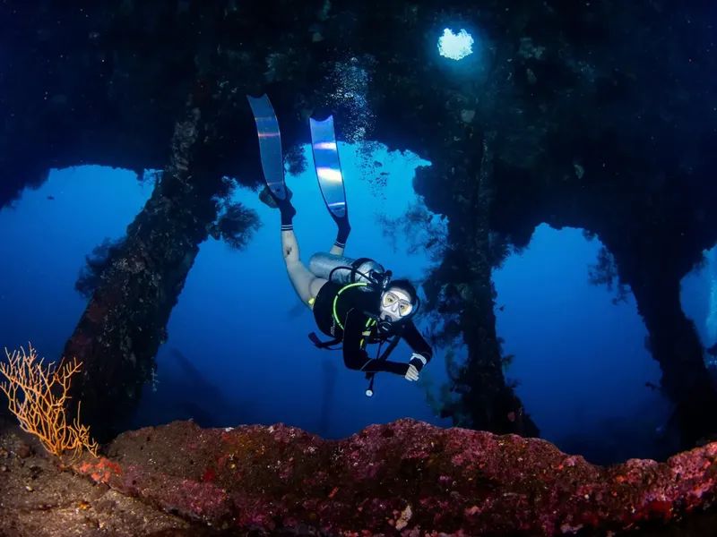 Plongeuse explorant une épave sous-marine avec une lumière vive